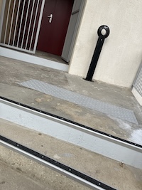 En haut de l'escalier, on voit sur le palier la bande d'éveil et un mètre plus loin, la porte d'entrée avec une marche non signalée.